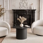Schräge Ansicht des modernen runden Couchtisches Linnea (Ø 70 cm) in Schwarz Matt mit markanter Säule in Lamellen-Optik, freigestellt auf weißem Hintergrund.