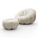 Klassische Ansicht des eleganten Drehsessels ORIA mit Hocker aus beigefarbenem Bouclé-Material, freigestellt auf einem neutralen, weißen Hintergrund.