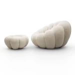 Klassische Ansicht des eleganten Drehsessels ORIA mit Hocker aus beigefarbenem Bouclé-Material, freigestellt auf einem neutralen, weißen Hintergrund.