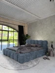 Einladendes Schlafzimmer-Ambiente mit dem blauen Polsterbett 180x200 Cloudi im samtigen Bezug Lumo (Chenille), stilvoll dekoriert mit grauer Bettwäsche und Kuscheldecke.