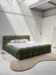 Schräge Ansicht des französischen Polsterbetts DIEGO (160x200 cm) in Coral 20 Bouclé, stilvoll arrangiert und harmonisch integriert in eine moderne Schlafzimmerumgebung.