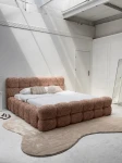 Schräge Ansicht des französischen Polsterbetts DIEGO (160x200 cm) in Coral 45 Bouclé, stilvoll arrangiert und harmonisch integriert in eine moderne Schlafzimmerumgebung.