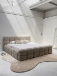 Schräge Ansicht des französischen Polsterbetts DIEGO (160x200 cm) in Coral 50 Bouclé, stilvoll arrangiert und harmonisch integriert in eine moderne Schlafzimmerumgebung.