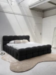 Schräge Ansicht des französischen Polsterbetts DIEGO (160x200 cm) in Coral 60 Bouclé, stilvoll arrangiert und harmonisch integriert in eine moderne Schlafzimmerumgebung.