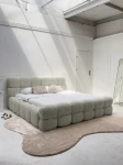 Schräge Ansicht des französischen Polsterbetts DIEGO (160x200 cm) in Coral 65 Bouclé, stilvoll arrangiert und harmonisch integriert in eine moderne Schlafzimmerumgebung.