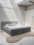 Schräge Ansicht des französischen Polsterbetts DIEGO (160x200 cm) in Coral 75 Bouclé, stilvoll arrangiert und harmonisch integriert in eine moderne Schlafzimmerumgebung.