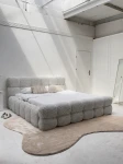 Schräge Ansicht des französischen Polsterbetts DIEGO (160x200 cm) in Coral 85 Bouclé, stilvoll arrangiert und harmonisch integriert in eine moderne Schlafzimmerumgebung.