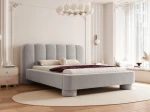 Schräge Ansicht des Designer-Polsterbettes Panola (180x200 cm) im hellen Bezug, die das Paneel-Kopfteil und die zylindrischen Beine zeigt, elegant arrangiert in einem hellen Schlafzimmer mit Stuck und einem ovalen Teppich. im ABRIAMO_06