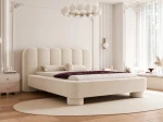 Schräge Ansicht des Designer-Polsterbettes Panola (180x200 cm) im hellen Bezug, die das Paneel-Kopfteil und die zylindrischen Beine zeigt, elegant arrangiert in einem hellen Schlafzimmer mit Stuck und einem ovalen Teppich. im NOW_OR_NEVER_02