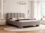 Schräge Ansicht des Designer-Polsterbettes Panola (180x200 cm) im hellen Bezug, die das Paneel-Kopfteil und die zylindrischen Beine zeigt, elegant arrangiert in einem hellen Schlafzimmer mit Stuck und einem ovalen Teppich. im RUNO_16