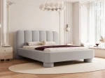 Schräge Ansicht des Designer-Polsterbettes Panola (180x200 cm) im hellen Bezug, die das Paneel-Kopfteil und die zylindrischen Beine zeigt, elegant arrangiert in einem hellen Schlafzimmer mit Stuck und einem ovalen Teppich. im RUNO_82