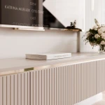 Nahaufnahme des TV-Lowboards SELIA, welche das elegante Design der drei geriffelten Rillenfronten in Kaschmir und die edlen Goldakzente im Detail präsentiert.