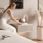 Frau sitzt auf dem Bett im Schlafzimmer neben dem hängenden Kaschmir-Nachttisch EVO mit geriffelter Front.