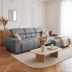 Das gemütliche Ecksofa Aldo im grauen Stoff Salvador 14, perfekt in Szene gesetzt in einem eleganten und lichtdurchfluteten Wohnzimmer.